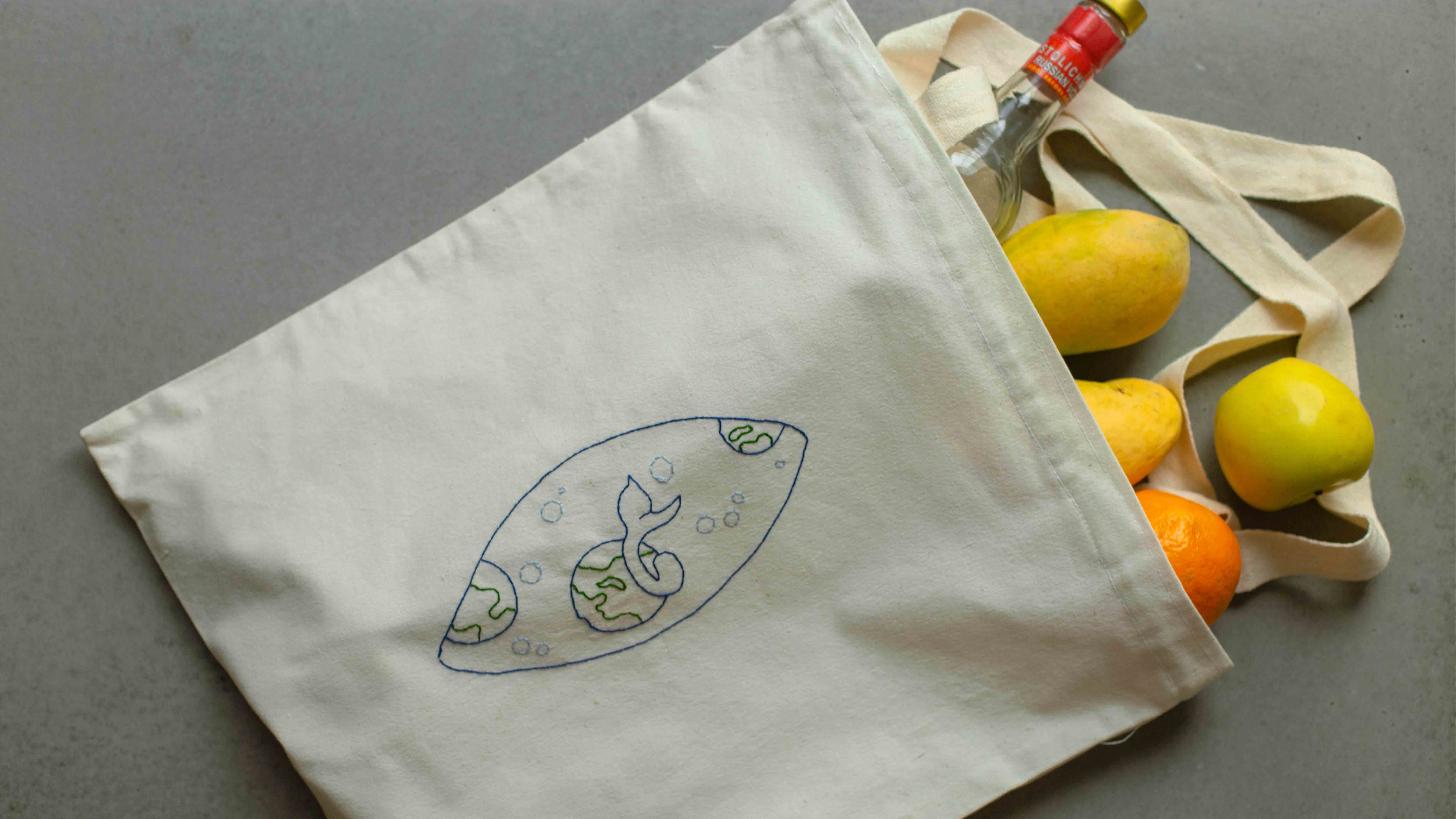 A natural canvas tote bag printed with a fine line-drawn logo, packed with lemons, an orange and a bottle